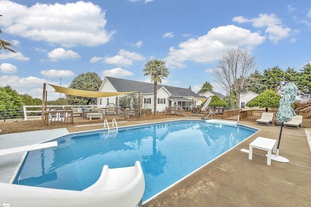 view of swimming pool featuring a wooden deck, a diving board, a water slide, and a patio area