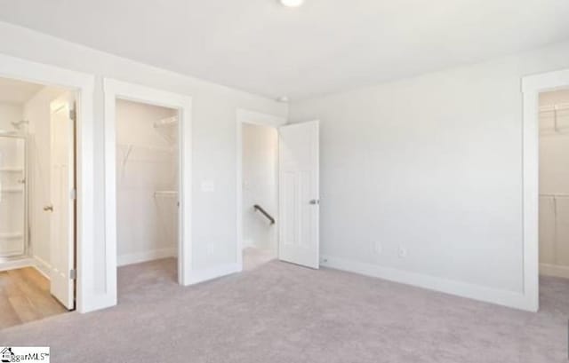 unfurnished bedroom with light carpet, connected bathroom, a walk in closet, and a closet