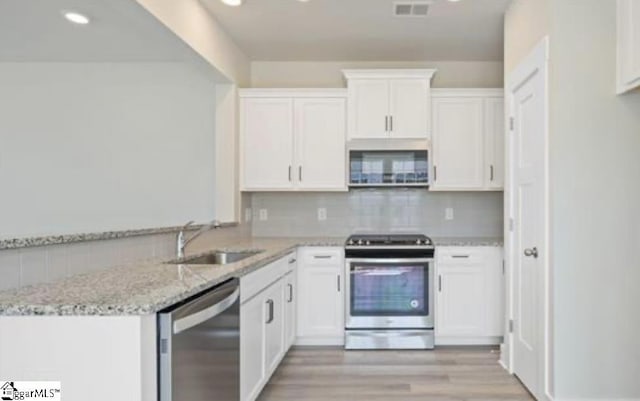 kitchen with tasteful backsplash, sink, white cabinets, light stone counters, and stainless steel appliances