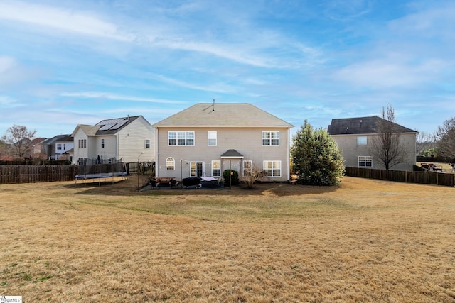 rear view of house featuring a trampoline and a lawn