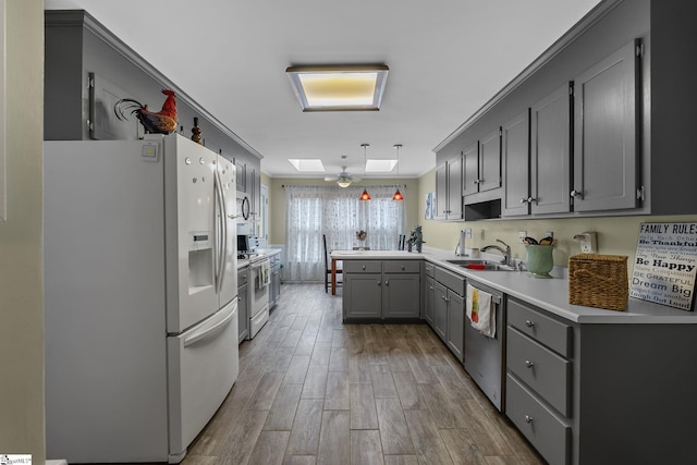 kitchen featuring sink, a skylight, gray cabinets, kitchen peninsula, and white appliances