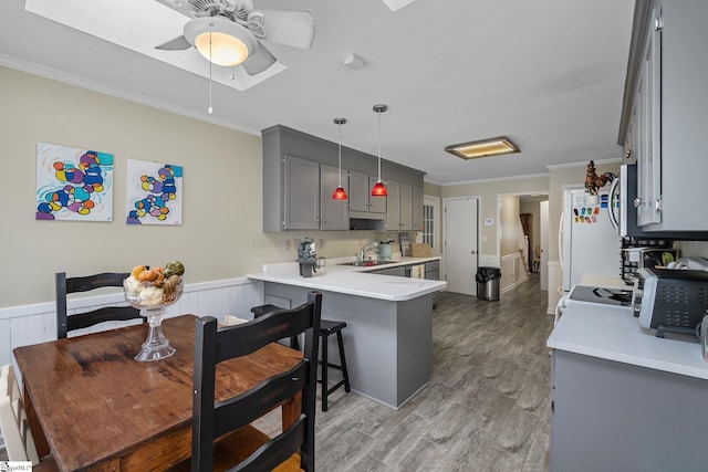 kitchen featuring gray cabinetry, decorative light fixtures, ornamental molding, a kitchen breakfast bar, and kitchen peninsula