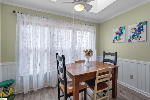 dining space featuring wood-type flooring, ornamental molding, ceiling fan, and a skylight