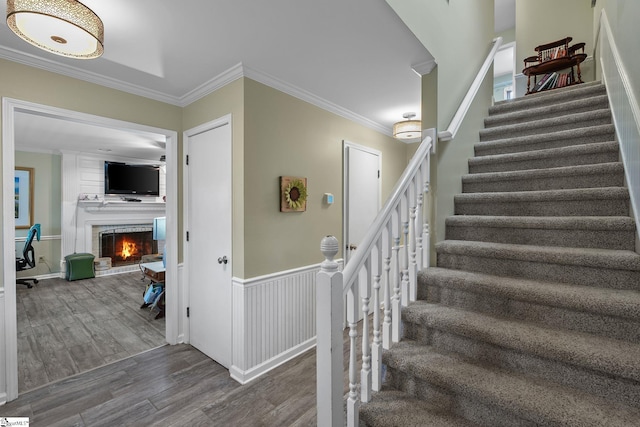 stairway featuring wood-type flooring, a fireplace, and crown molding