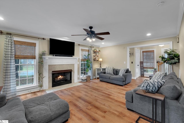 living room featuring ceiling fan, ornamental molding, a tiled fireplace, and light hardwood / wood-style flooring