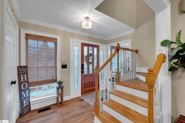 foyer entrance with a notable chandelier, ornamental molding, light hardwood / wood-style flooring, and a wealth of natural light