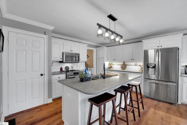 kitchen featuring sink, white cabinetry, ornamental molding, appliances with stainless steel finishes, and a kitchen island with sink