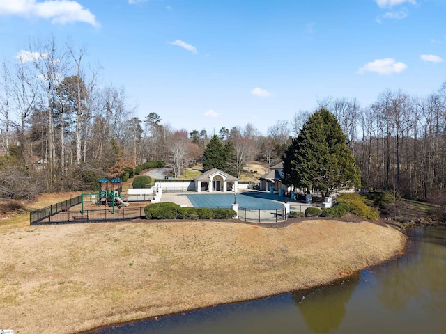 exterior space with a playground, a water view, a covered pool, and a lawn