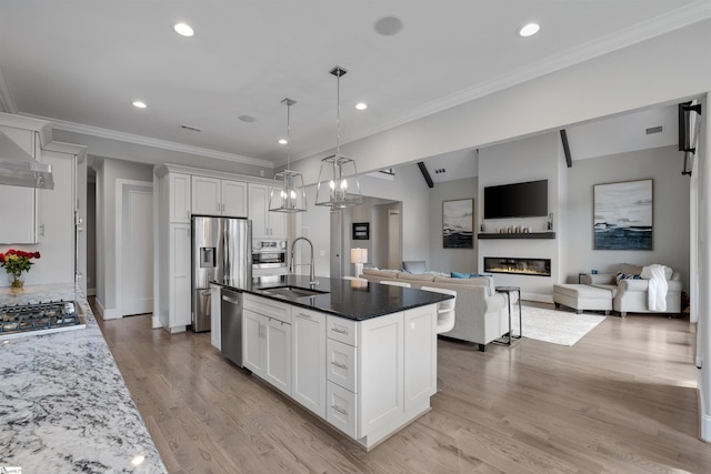 kitchen featuring decorative light fixtures, sink, white cabinets, stainless steel appliances, and a center island with sink