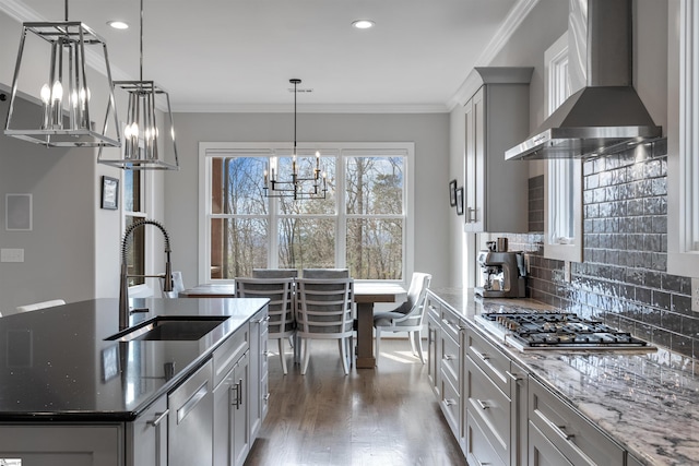 kitchen featuring sink, dark stone countertops, appliances with stainless steel finishes, pendant lighting, and wall chimney range hood