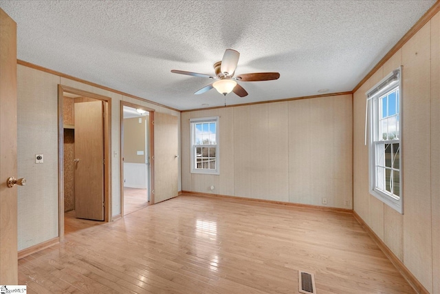 spare room with crown molding, plenty of natural light, a textured ceiling, and light wood-type flooring