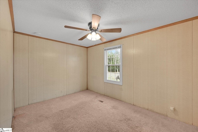 carpeted empty room with ceiling fan, ornamental molding, and a textured ceiling