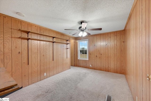 empty room with ceiling fan, wooden walls, carpet floors, and a textured ceiling