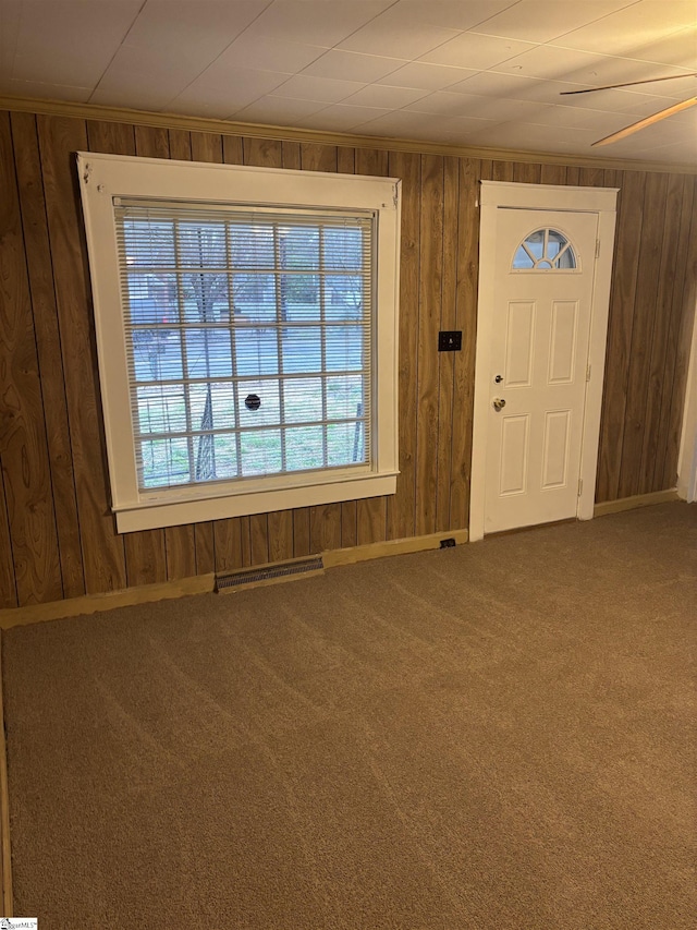 carpeted foyer featuring crown molding and wooden walls