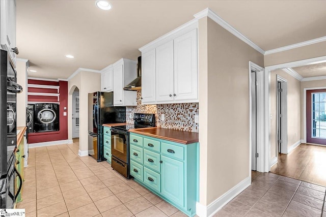 kitchen with black appliances, washer and dryer, ornamental molding, wall chimney range hood, and white cabinets