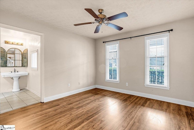 empty room featuring ceiling fan, sink, a textured ceiling, and light hardwood / wood-style flooring