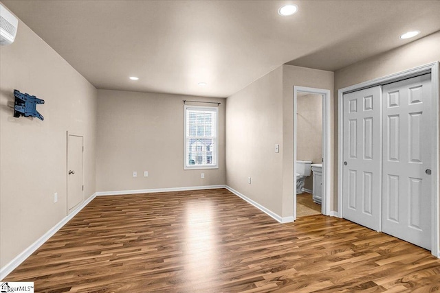 unfurnished bedroom featuring hardwood / wood-style floors, ensuite bath, and a closet