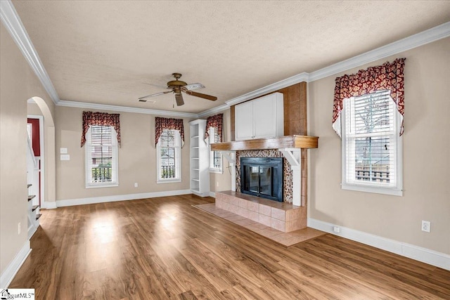 unfurnished living room with a fireplace, wood-type flooring, ornamental molding, ceiling fan, and a textured ceiling