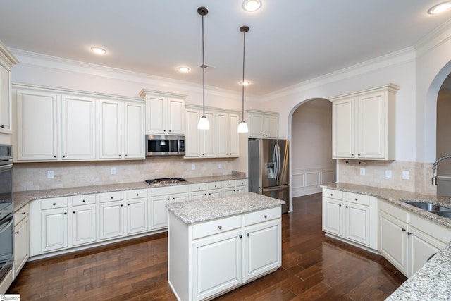 kitchen with sink, appliances with stainless steel finishes, light stone countertops, a kitchen island, and decorative light fixtures