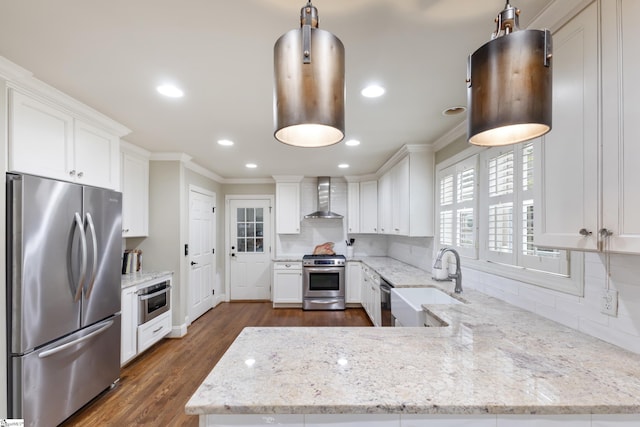 kitchen featuring appliances with stainless steel finishes, pendant lighting, sink, white cabinets, and wall chimney exhaust hood