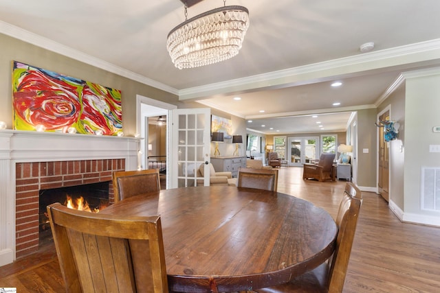 dining area featuring crown molding, hardwood / wood-style flooring, a notable chandelier, a brick fireplace, and french doors