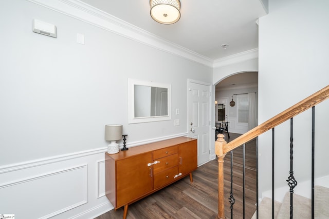 hallway featuring arched walkways, a wainscoted wall, dark wood-style flooring, stairway, and crown molding