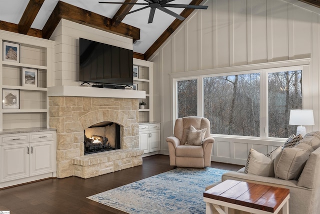 living room with a stone fireplace, lofted ceiling with beams, dark hardwood / wood-style flooring, built in features, and ceiling fan