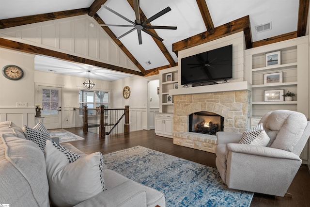 living room with dark hardwood / wood-style floors, a stone fireplace, built in features, and vaulted ceiling with beams