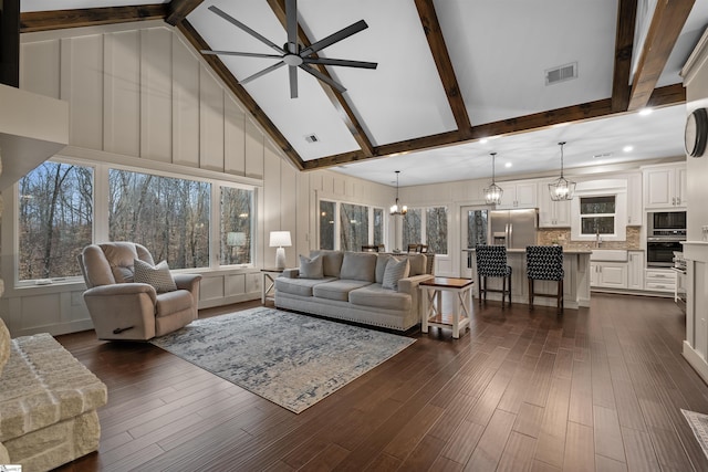 living room featuring dark hardwood / wood-style flooring, ceiling fan with notable chandelier, beam ceiling, and high vaulted ceiling