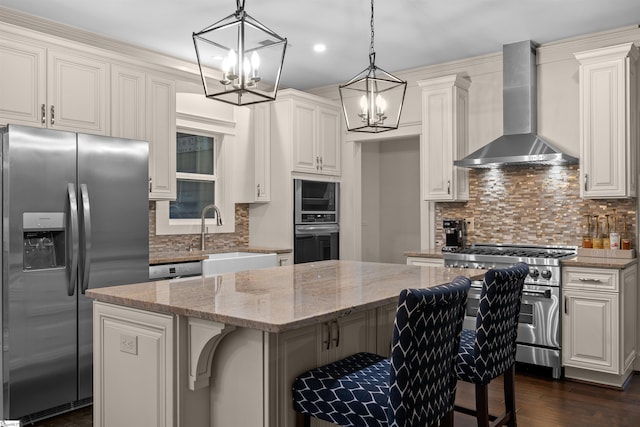 kitchen featuring wall chimney range hood, a breakfast bar, stainless steel appliances, a center island, and white cabinets