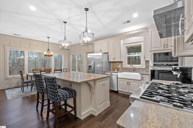 kitchen featuring appliances with stainless steel finishes, pendant lighting, sink, a center island, and light stone countertops