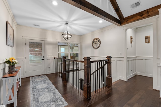 entrance foyer with ornamental molding, dark wood-type flooring, an inviting chandelier, and beam ceiling