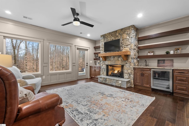 living room with a stone fireplace, dark hardwood / wood-style floors, beverage cooler, crown molding, and bar area