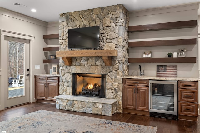 bar with wine cooler, a stone fireplace, crown molding, light stone counters, and dark hardwood / wood-style flooring