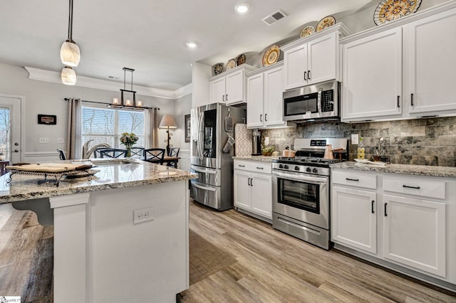 kitchen with a breakfast bar, white cabinetry, hanging light fixtures, a center island with sink, and stainless steel appliances