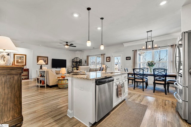 kitchen featuring appliances with stainless steel finishes, an island with sink, white cabinets, hanging light fixtures, and light stone countertops