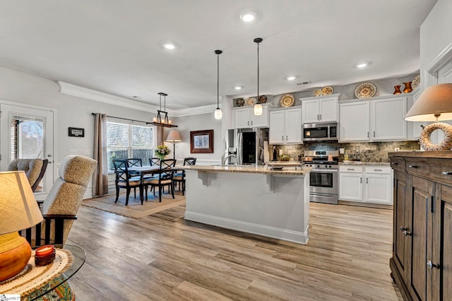 kitchen with pendant lighting, a breakfast bar, stainless steel appliances, white cabinets, and a center island with sink