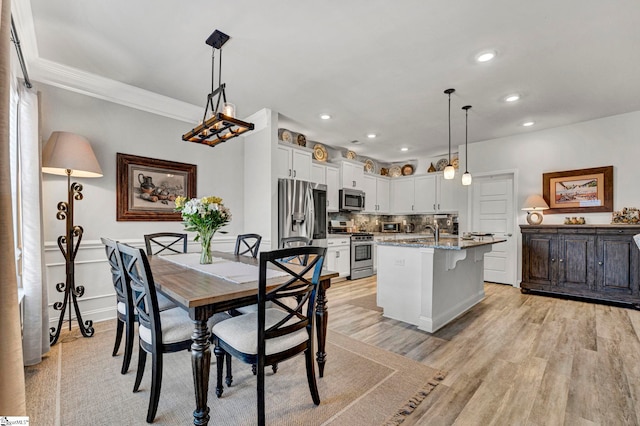 kitchen featuring hanging light fixtures, stainless steel appliances, light stone counters, white cabinets, and a center island with sink