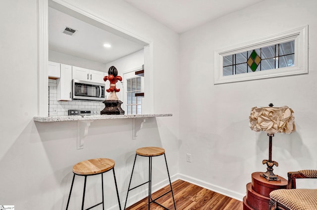 kitchen featuring a kitchen breakfast bar, light stone countertops, white cabinets, dark hardwood / wood-style flooring, and decorative backsplash