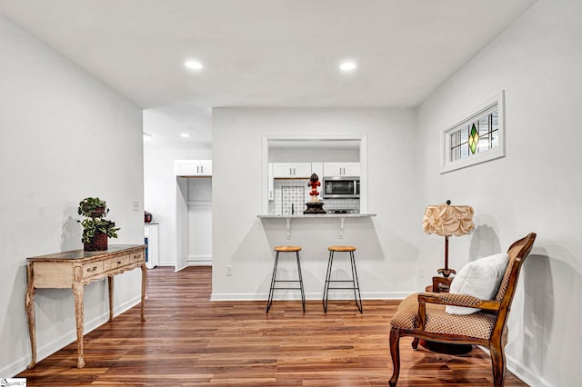 kitchen featuring a breakfast bar area, white cabinets, decorative backsplash, kitchen peninsula, and dark wood-type flooring