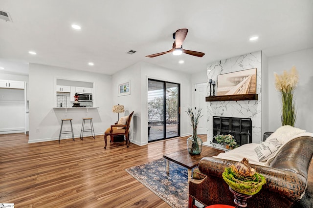 living room featuring a high end fireplace, light hardwood / wood-style flooring, and ceiling fan