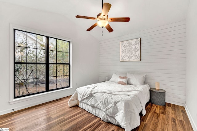 bedroom featuring lofted ceiling, wood-type flooring, wooden walls, and ceiling fan