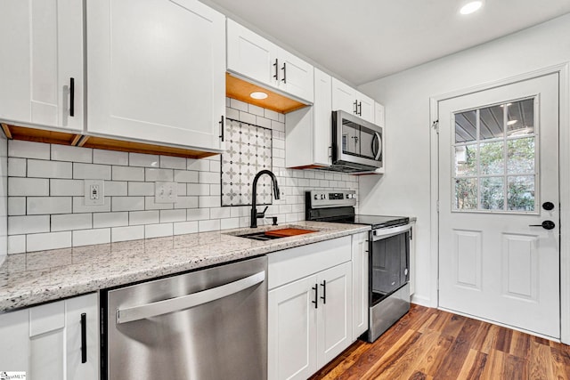 kitchen featuring sink, stainless steel appliances, light stone counters, wood-type flooring, and white cabinets