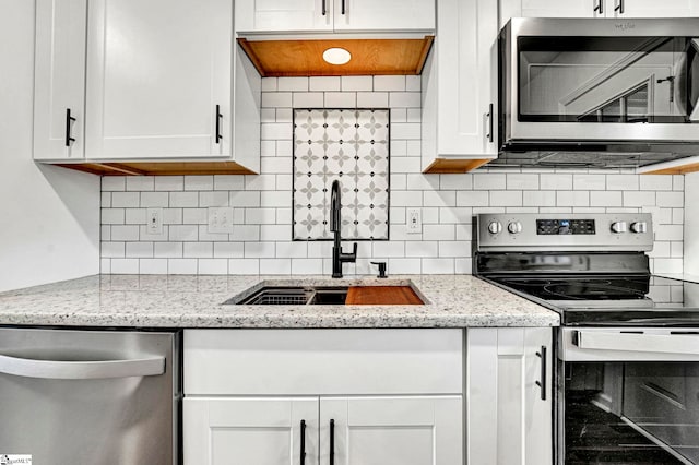 kitchen with white cabinetry, sink, light stone countertops, and appliances with stainless steel finishes