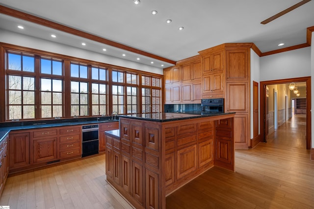 kitchen featuring light hardwood / wood-style flooring, dark stone counters, a kitchen island, oven, and beamed ceiling