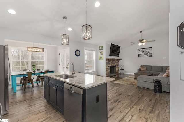 kitchen with sink, light stone counters, decorative light fixtures, stainless steel appliances, and a kitchen island with sink