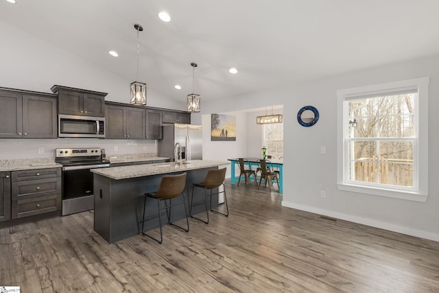 kitchen featuring dark brown cabinetry, decorative light fixtures, a kitchen breakfast bar, an island with sink, and stainless steel appliances