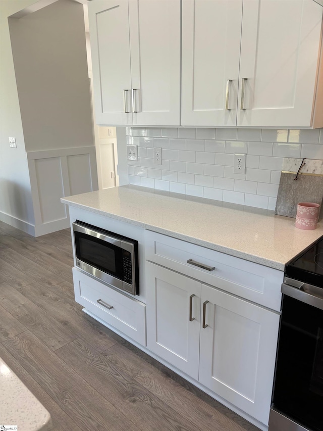 kitchen featuring white cabinetry, stainless steel microwave, light stone counters, and light hardwood / wood-style flooring