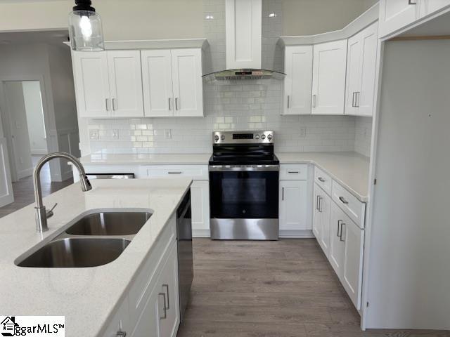 kitchen featuring pendant lighting, wall chimney range hood, sink, white cabinetry, and stainless steel electric range oven