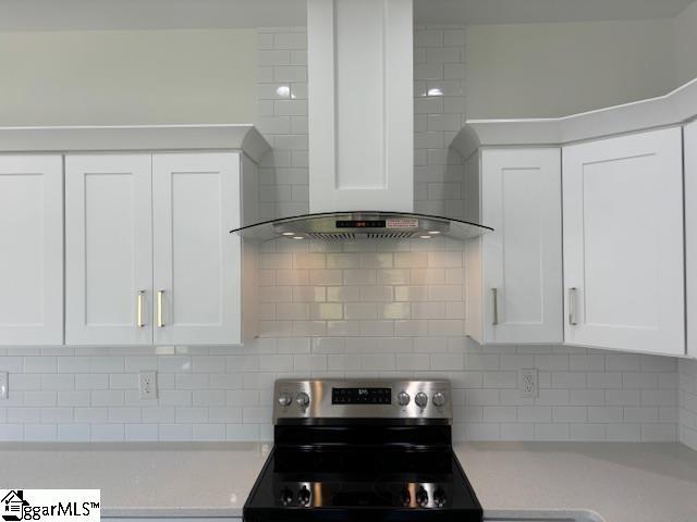 kitchen with tasteful backsplash, wall chimney range hood, white cabinets, and stainless steel electric range oven